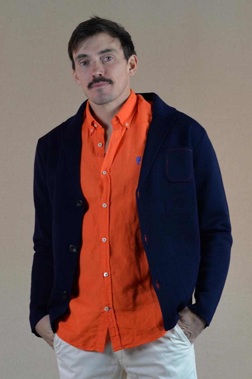 Homme de face présentant un style élégant avec un cardigan bleu marine, chemise en lin orange.