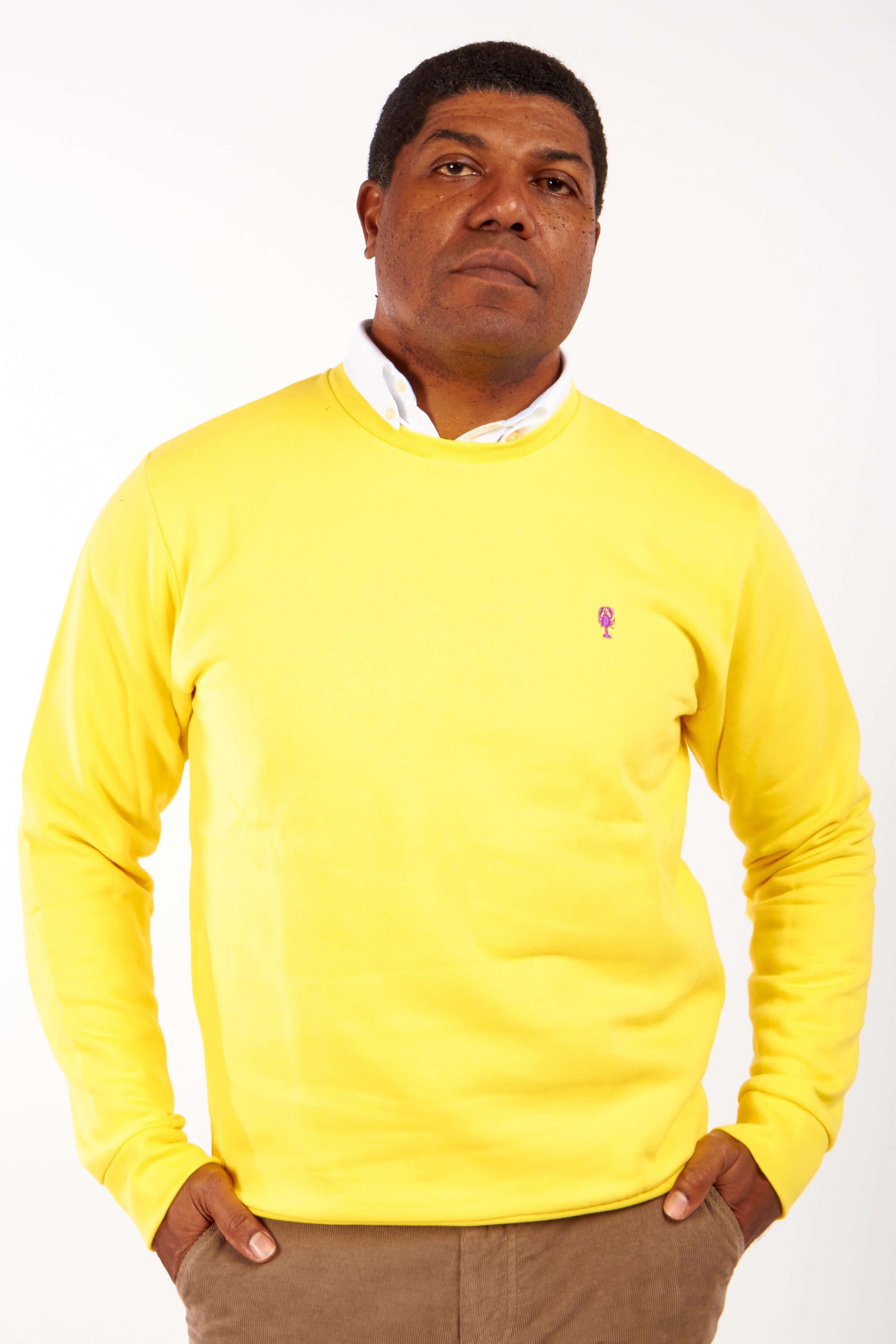 Homme de face portant un sweatshirt jaune brodé d'un homard violet.