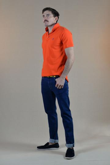 Homme de profil portant un jeans bleu brode d'un petit homard rouge et un polo col mao orange.